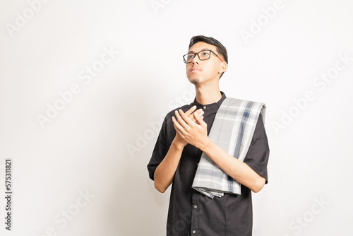 A male single model doing pray with his two hands held together and looking up. Indonesian or southeast asian. Studio photoshoot with white background.