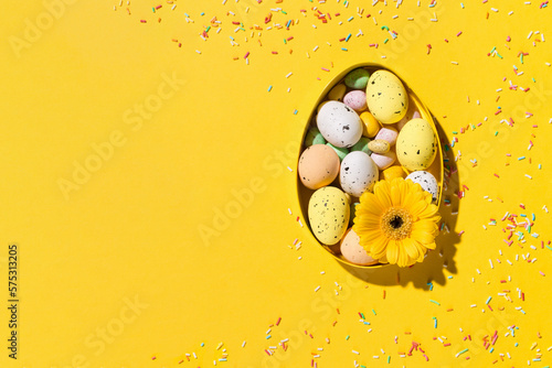 Spring Easter card concept. Yellow, pink, blue and white easter eggs, daisy flowers on paper yellow background.