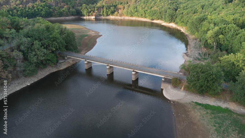 Aerial view of a bridge crossing a lake in summer, surrounded by the green forest and fields.