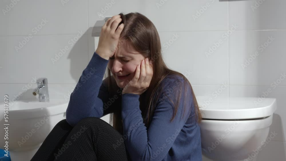 Crying woman suffering from depression sitting on floor in bathroom at home. Concept of depression, suicide, stress, mental illness, loneliness and frustration Crying woman suffering from depression sitting on floor in bathroom at home. Concept of depression, suicide, stress, mental illness, loneliness and frustration
