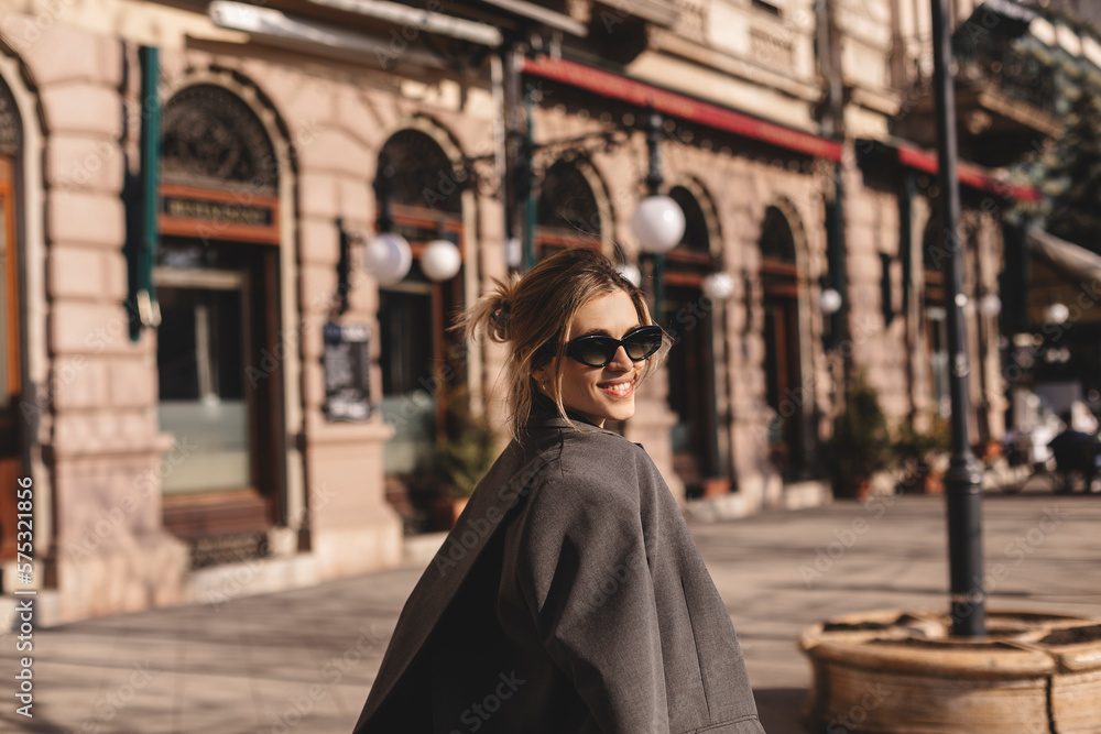 Young beautiful smiling hipster woman in trendy outfit. Sexy carefree woman posing on the street. Cheerful and happy in black sunglasses and grey suit turn around. Lifestyle, female beauty concept. Young beautiful smiling hipster woman in trendy outfit. Sexy carefree woman posing on the street. Cheerful and happy in black sunglasses and grey suit turn around. Lifestyle, female beauty concept.