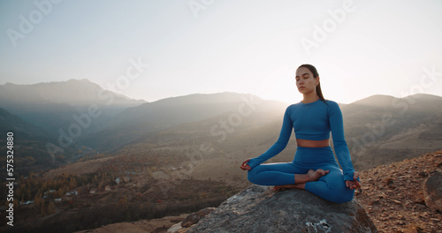 Fit girl doing lotus pose. Young athletic woman meditating in mountains, training and relaxing during sunrise - active lifestyle, zen concept 