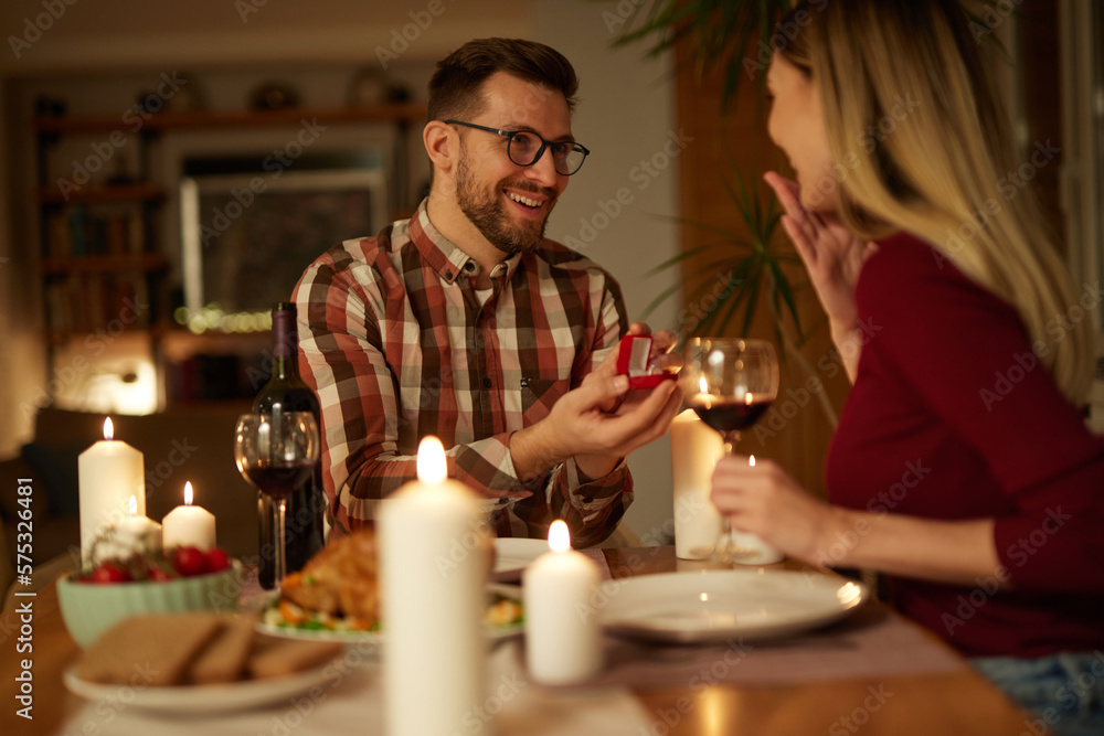 Delighted woman looking at her boyfriend while getting a marriage proposal over romantic dinner at home