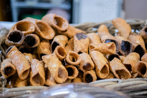 Sweet empty fried cannoli without filling in basket on counter at food market. Pastry, dessert, culinary, italian sweet food and confectionery concept photo