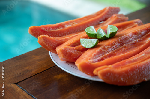 Sliced papaya with lime on table near swimming pool