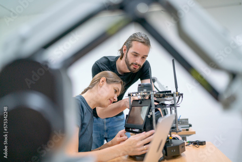 Caucasian professional engineer or technician workers with casual cloth help to check and maintenance small robotic machine that put on table in factory workplace.