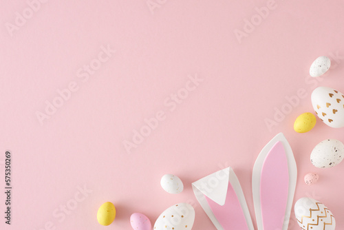 Easter celebration concept. Top view photo of yellow pink white eggs easter bunny ears on isolated pastel pink background with empty space. Holiday card idea