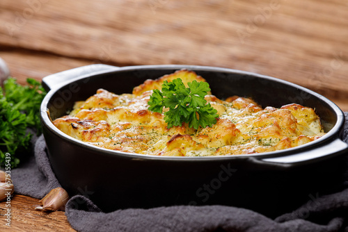 Potato casserole with cheese and parsley on wooden table. French cuisine, close up. Free space for text