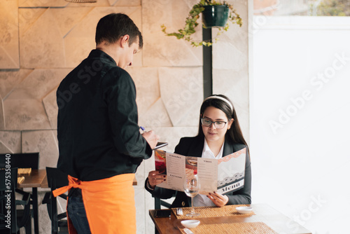 The waiter is taking the order in his restaurant.  An executive woman is ordering a waiter at a restaurant.