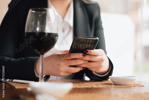 Hands of a white woman typing on a cell phone inside a fancy restaurant. Hands of an executive woman chatting inside a restaurant.