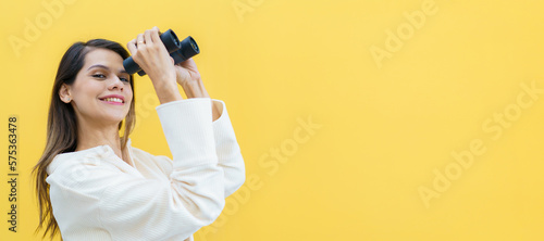 Beautiful caucasian white young woman looking through the twin lens binocular. Woman using binocular portrait on yellow background.