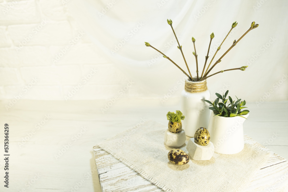 Branches in buds and young leaves in a vase in the interior. Composition of quail egg and green moss on a stand. The idea of festive decoration of the room for Easter. High quality photo