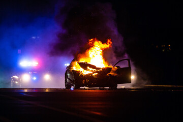 Car on fire at night with police lights in background