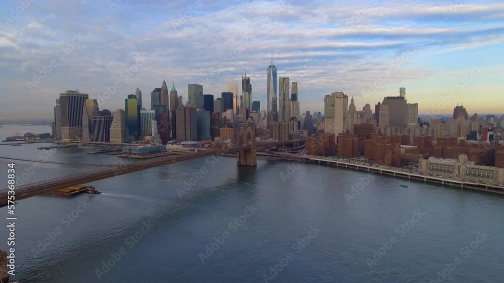 Aerial Shot Of Tall Modern Buildings Against Sky, Drone Panning Over East River With Brooklyn Bridge In City - New York, New York Aerial Shot Of Tall Modern Buildings Against Sky, Drone Panning Over East River With Brooklyn Bridge In City - New York, New York