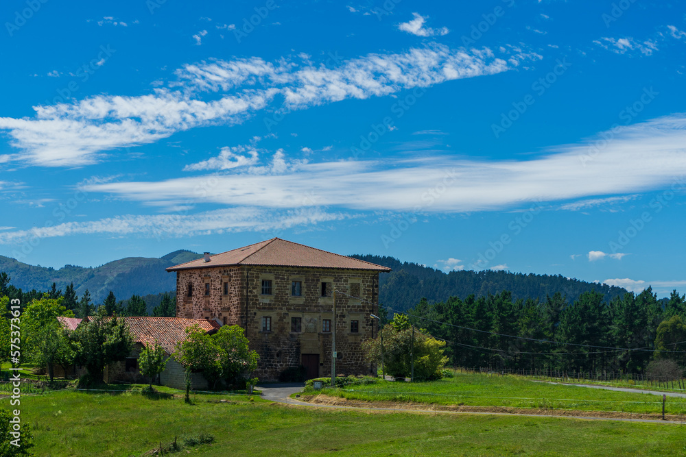 An old brick manor a tiled roof against the backdrop of mountains and green grass. Basque Country, Spain. An old brick manor a tiled roof against the backdrop of mountains and green grass. Basque Country, Spain.