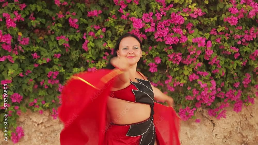 A young brunette in a red suit dances against the backdrop of blooming bougainvilleas oriental dance playing with a large headscarf A young brunette in a red suit dances against the backdrop of blooming bougainvilleas oriental dance playing with a large headscarf