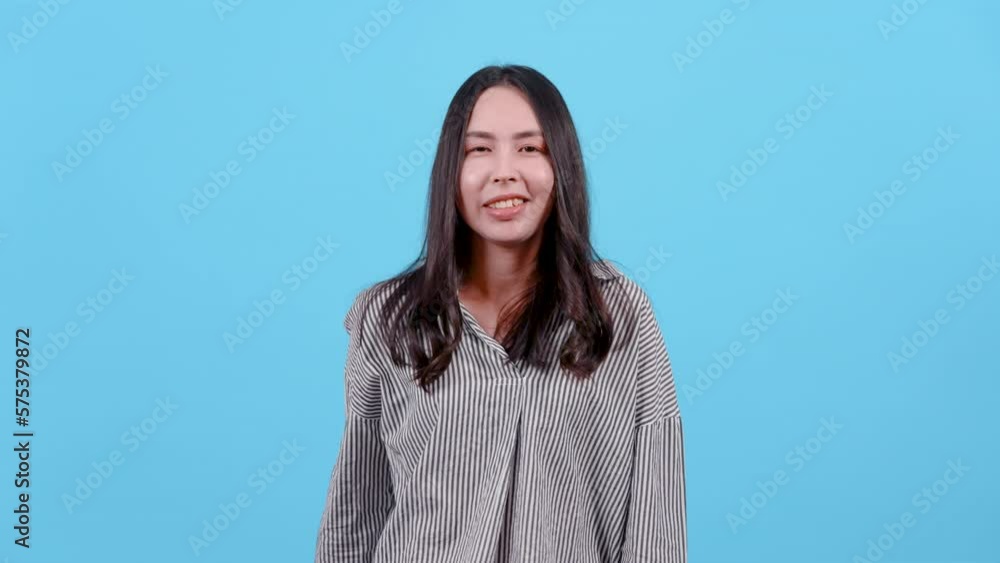 4K, Asian woman with long hair wearing black white striped shirt, Lightly clenched fists raised them high looks like someone happy about something, Isolated indoor studio on blue background. 4K, Asian woman with long hair wearing black white striped shirt, Lightly clenched fists raised them high looks like someone happy about something, Isolated indoor studio on blue background.