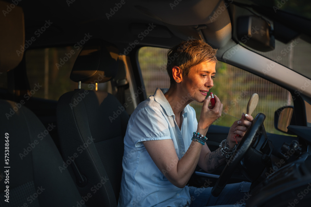 One woman mature caucasian female businesswoman sitting in car putting lipstick fixing repairing makeup on her face while waiting in summer day evening real people copy space gray hair One woman mature caucasian female businesswoman sitting in car putting lipstick fixing repairing makeup on her face while waiting in summer day evening real people copy space gray hair