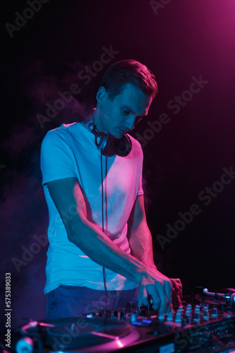 Cool young DJ playing music on party in blue neon lights. White male person performing as a disc jockey in night club