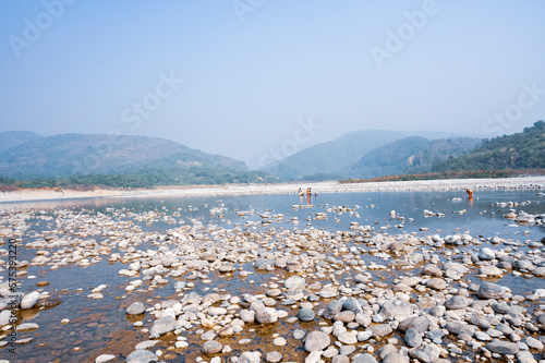 Pile of white stones on the shore of a lake with mountains in the background. ‍Sylhet, Bangladesh