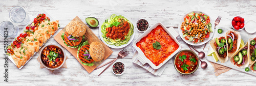 Healthy plant based vegetarian meal table scene. Overhead view on a white wood banner background. Jackfruit tacos, zucchini lasagna, walnut bolognese zoodles, chickpea burgers, hummus, soups, salad. photo