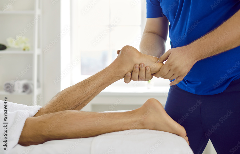 Obraz premium Close up of masseur massage client feet relieve painful feelings. Physiotherapist work with male customer legs pain relief in wellness studio or clinic. Healthcare and physiotherapy concept.