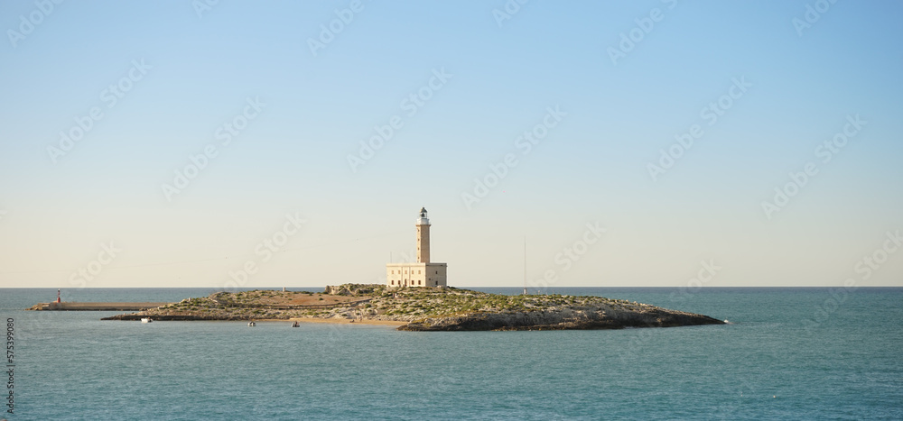 Small island with a lighthouse in the Adriatic Sea under a blue sky and calm water