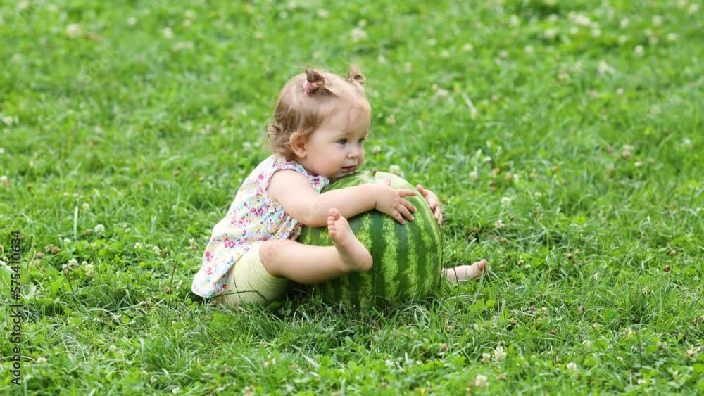 a happy little girl is sitting on the grass in summer with a big watermelon. Summer picnic. A child in nature in summer. 4K Video a happy little girl is sitting on the grass in summer with a big watermelon. Summer picnic. A child in nature in summer. 4K Video