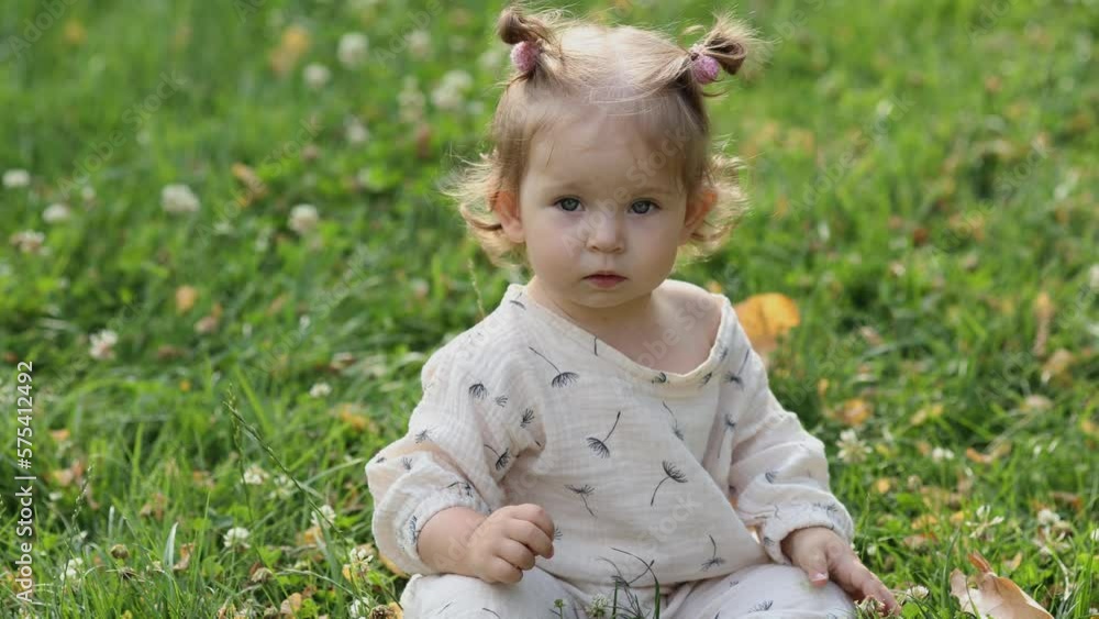 cute little girl in cotton clothes is sitting on the green grass in the park. cute little girl in cotton clothes is sitting on the green grass in the park.