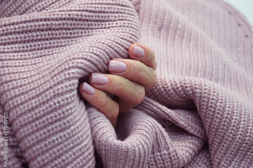 Women's hands with beautiful nails on the background of a pink sweater. Professional manicure. Knitted texture background.