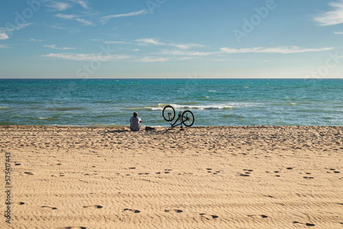 Man sitting on the sand looking out to sea after a long bike ride. Copy space on the sky or on the sand
