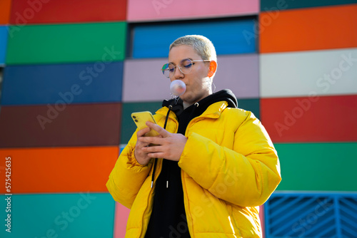 lgbt girl with short hair making bubble gum texting with smartphone yellow colors