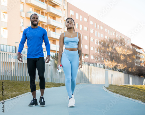 Healthy lifestyle concept. Dark-skinned millennial couple doing outdoor sports together, the man and woman walk through a park in autumn, the black girl with braids carries a bottle of water.