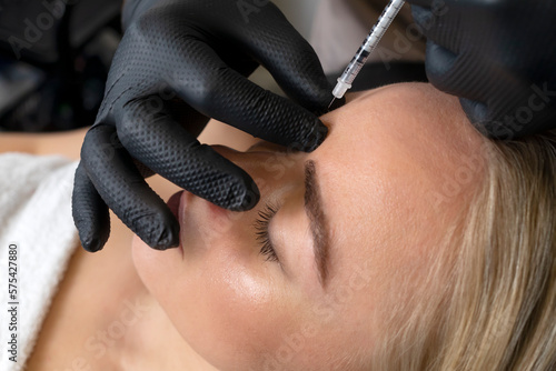 Closeup of Caucasian woman gets botox cosmetic injection in forehead. Beauty physician inserts needle of syringe into between the eyebrows, face of beautiful female. Cosmetologist, aesthetic medicine. photo