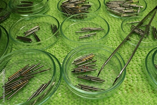 A look into dentist shelf - sorted dental stomatology burs, both diamond and carbide heads of various shapes, placed in shallow medical bowls on light green antislip surface with medical forceps.  photo