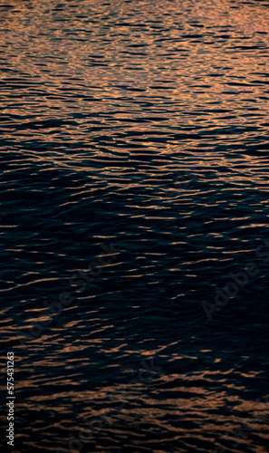 Background, ripples on the water in the rays of the setting sun. Undulating water surface.