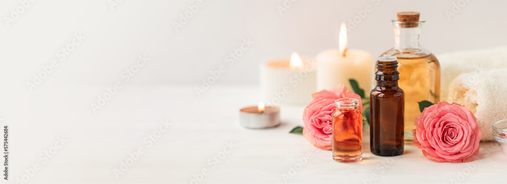 Aromatherapy. Pure organic essential rose oil concept. Elixir with plant based floral herbal ingredients. Pink flowers extract. Spa atmosphere with candle, towel. White background. Banner copy space Aromatherapy. Pure organic essential rose oil concept. Elixir with plant based floral herbal ingredients. Pink flowers extract. Spa atmosphere with candle, towel. White background. Banner copy space