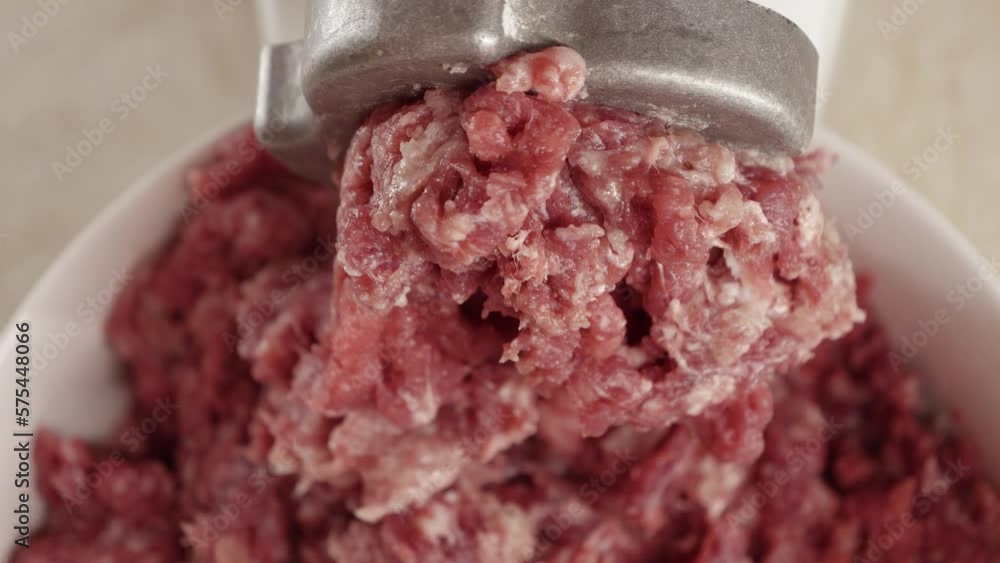 Closeup of minced meat coming out of electric grinder and falling in bowl. Cooking at home, kitchen appliance, healthy nutrition, hamburger ingredients Closeup of minced meat coming out of electric grinder and falling in bowl. Cooking at home, kitchen appliance, healthy nutrition, hamburger ingredients