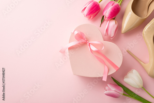 8-march celebration concept. Top view photo of pink heart shaped giftbox with ribbon bow tulips and beige high heel shoes on isolated pastel pink background