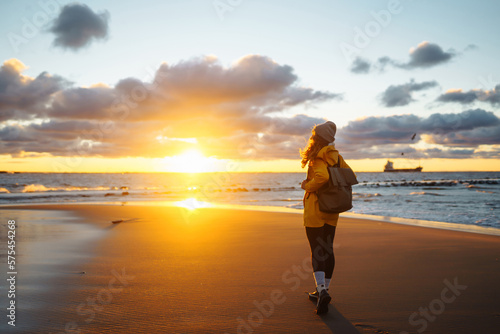Pretty female traveler walks on shore near tranquil sea at sunser. Nature paradise