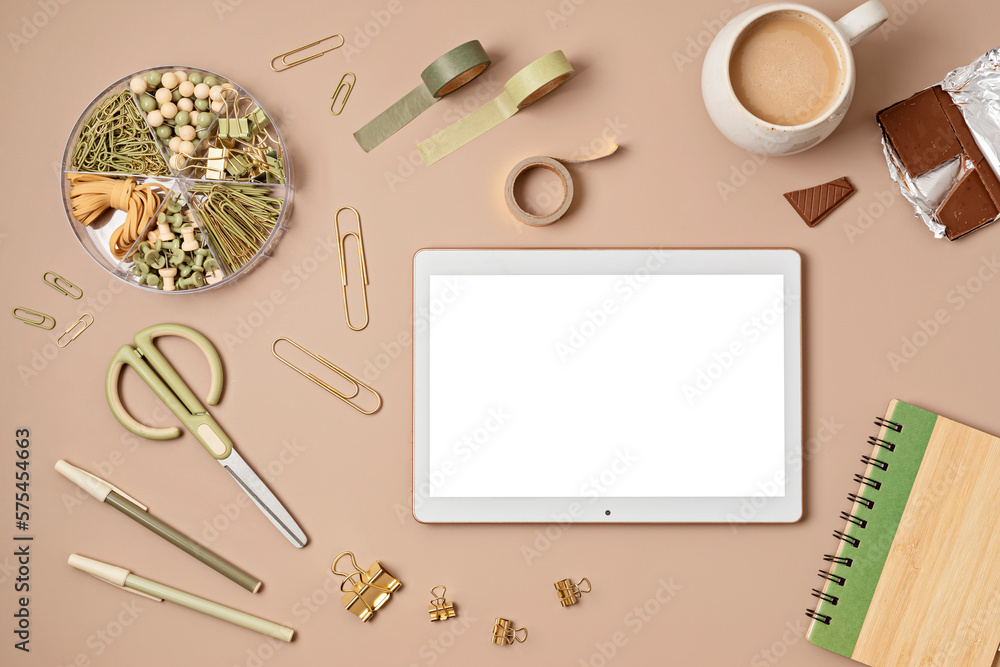 Mockup of pad or tablet computer and office supplies on beige background, with white screen copy space for your text. Flat lay, top view photo mock up.