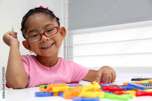4-year-old brunette Latina girl with autism spectrum disorder ASD like Asperger, Rett and Heller draws at a desk, plays with colors alone antisocial