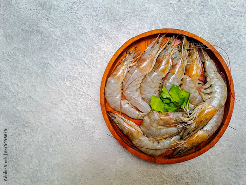 Raw prawns on a wooden plate isolated on gray background. Fresh shrimps ready to cook. Selective focus 