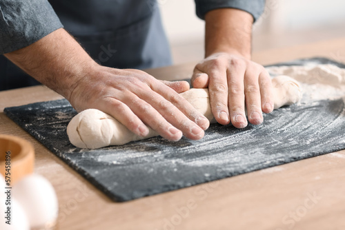 Male baker preparing dough at table in kitchen, closeup