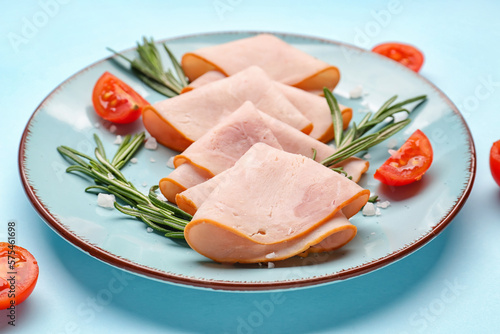 Plate with slices of tasty ham, tomatoes and rosemary on blue background