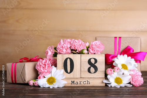 Cube calendar with date MARCH 8, beautiful flowers and gift boxes on wooden table. Women's Day celebration