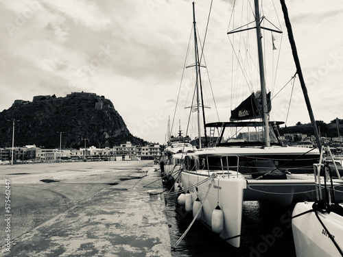 Black and white view of an Autumn noon at Nafplion port, Peloponnese, Greece with catamarans docked in line and the fortress of Palamidi in the background