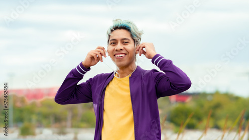 hombre joven moreno sonriente con audífonos ropa morada y amarilla con pelo pintado feliz 