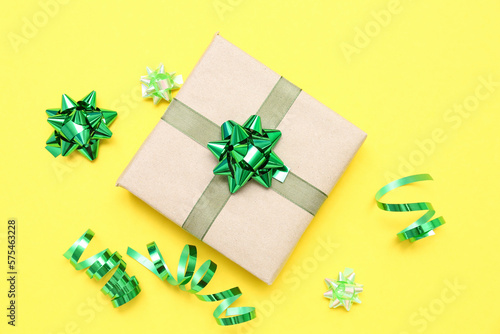 Gift box with green bows and serpentine on yellow background © Pixel-Shot