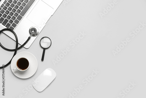 Laptop with magnifier, stethoscope and cup of coffee on grey background. World Health Day